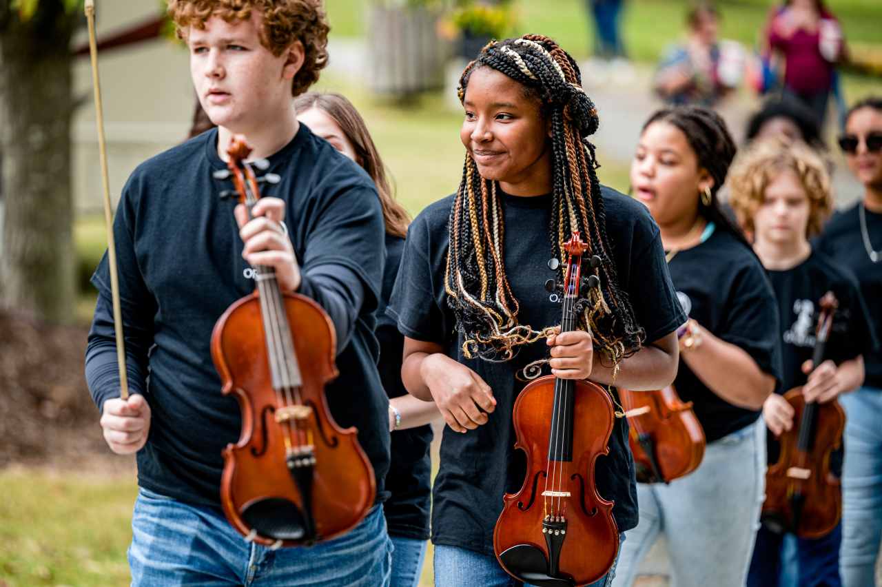 Suzuki Method Overview - teenagers holding violin and bow walking outdoor